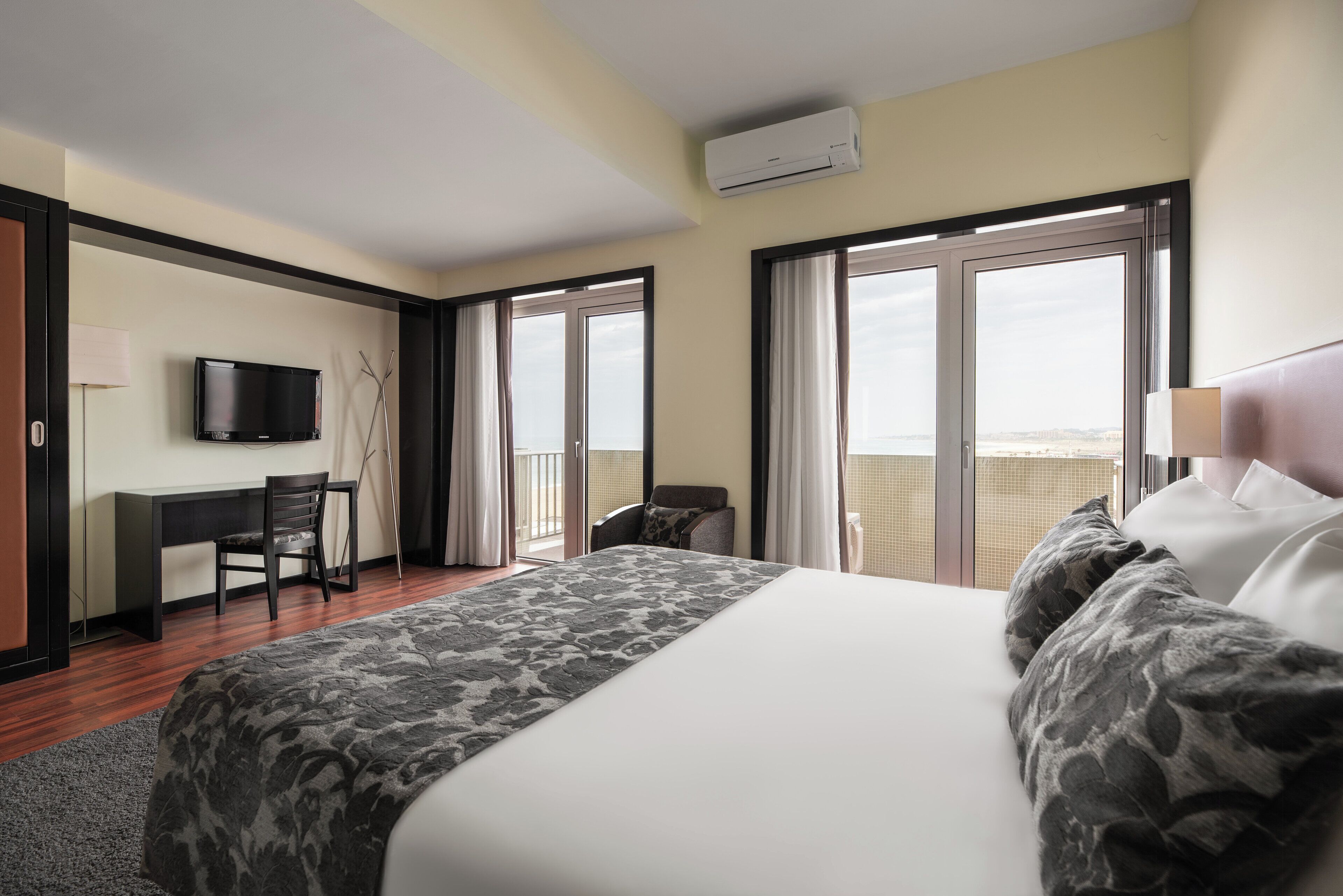 Habitación de hotel con una cama grande, un escritorio, una silla, un televisor y un balcón con vistas.