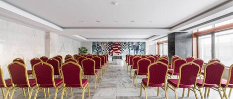 A conference room with rows of red chairs and gold frames, marble flooring, and a large window with a view.