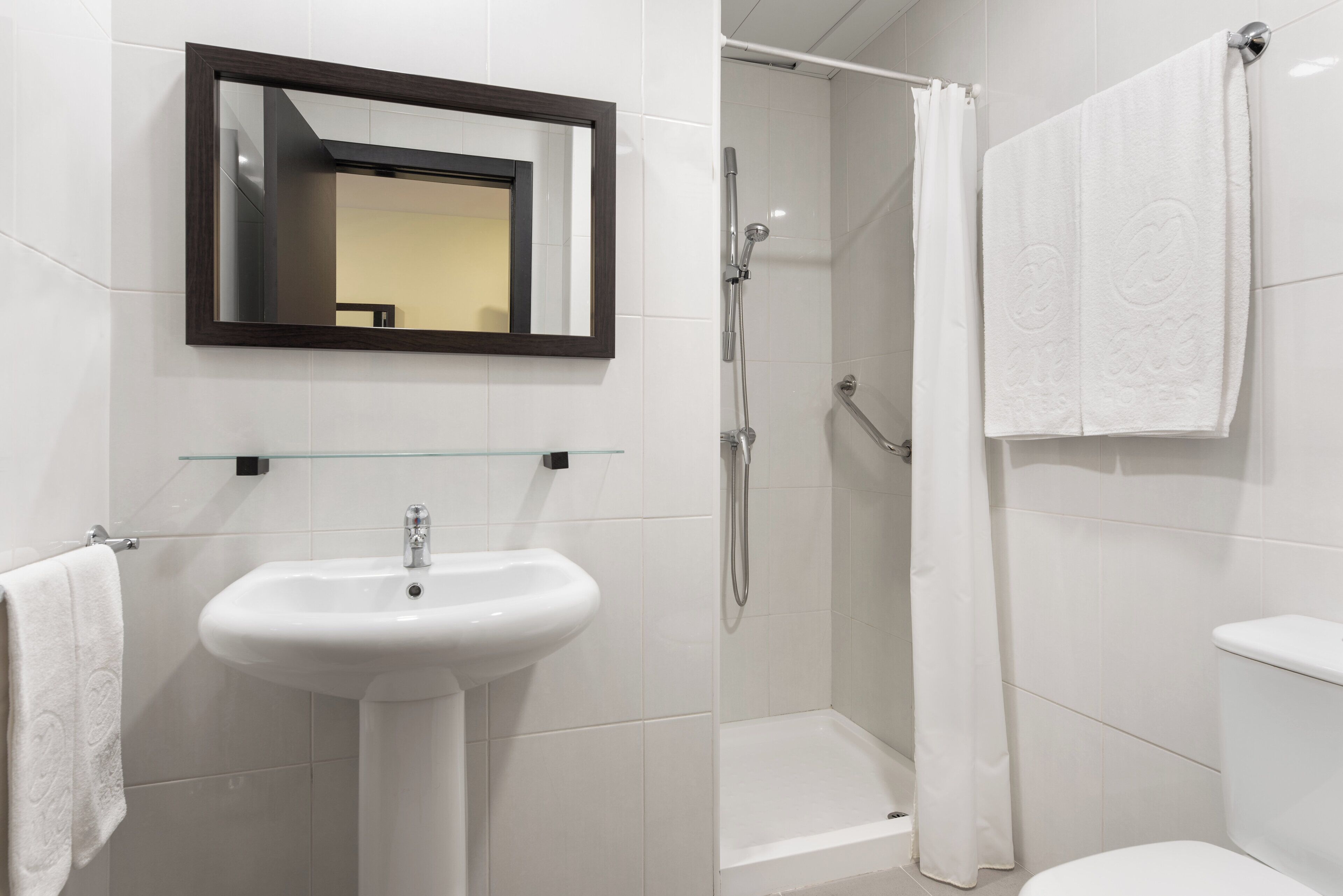 A bathroom with a white sink, a mirror, a shower with a glass door, and a toilet.
