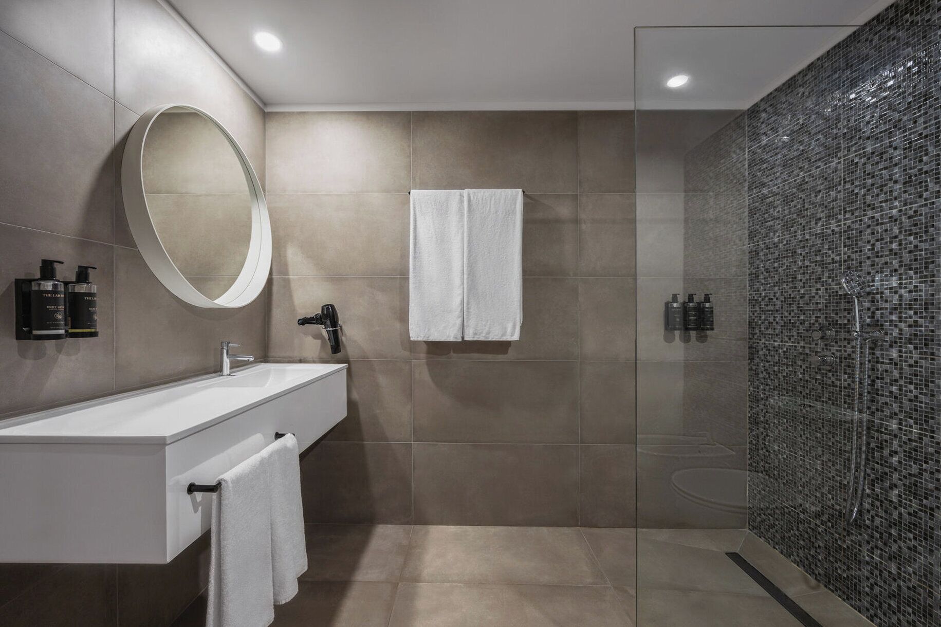 A modern bathroom with a sink, mirror, towel rack, and a glass-enclosed shower area.