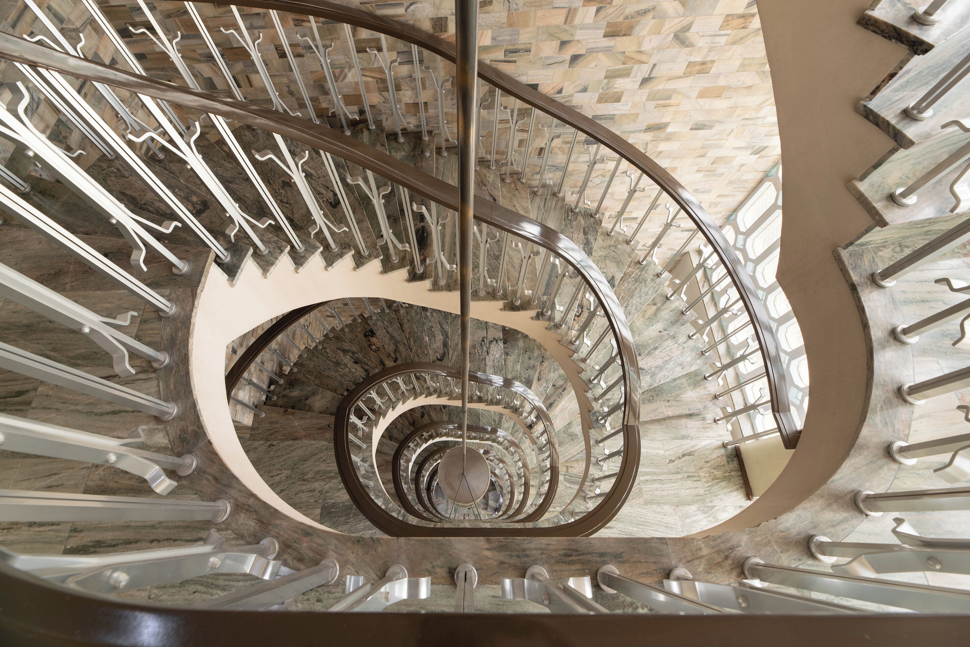 A spiral staircase with a circular design, metal railings, and a stone wall background.
