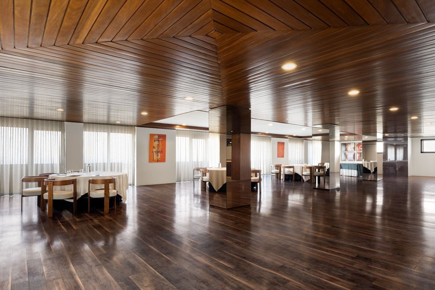 A spacious hotel lobby with wooden panel ceilings, multiple dining areas, and artwork on the walls.
