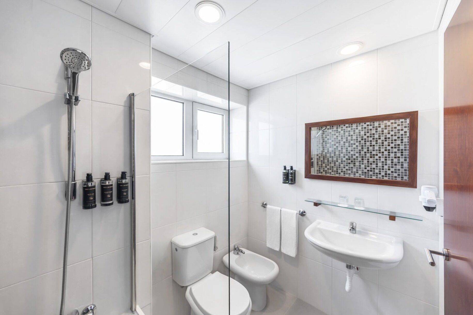 A modern bathroom with a shower, toilet, bidet, and two sinks.