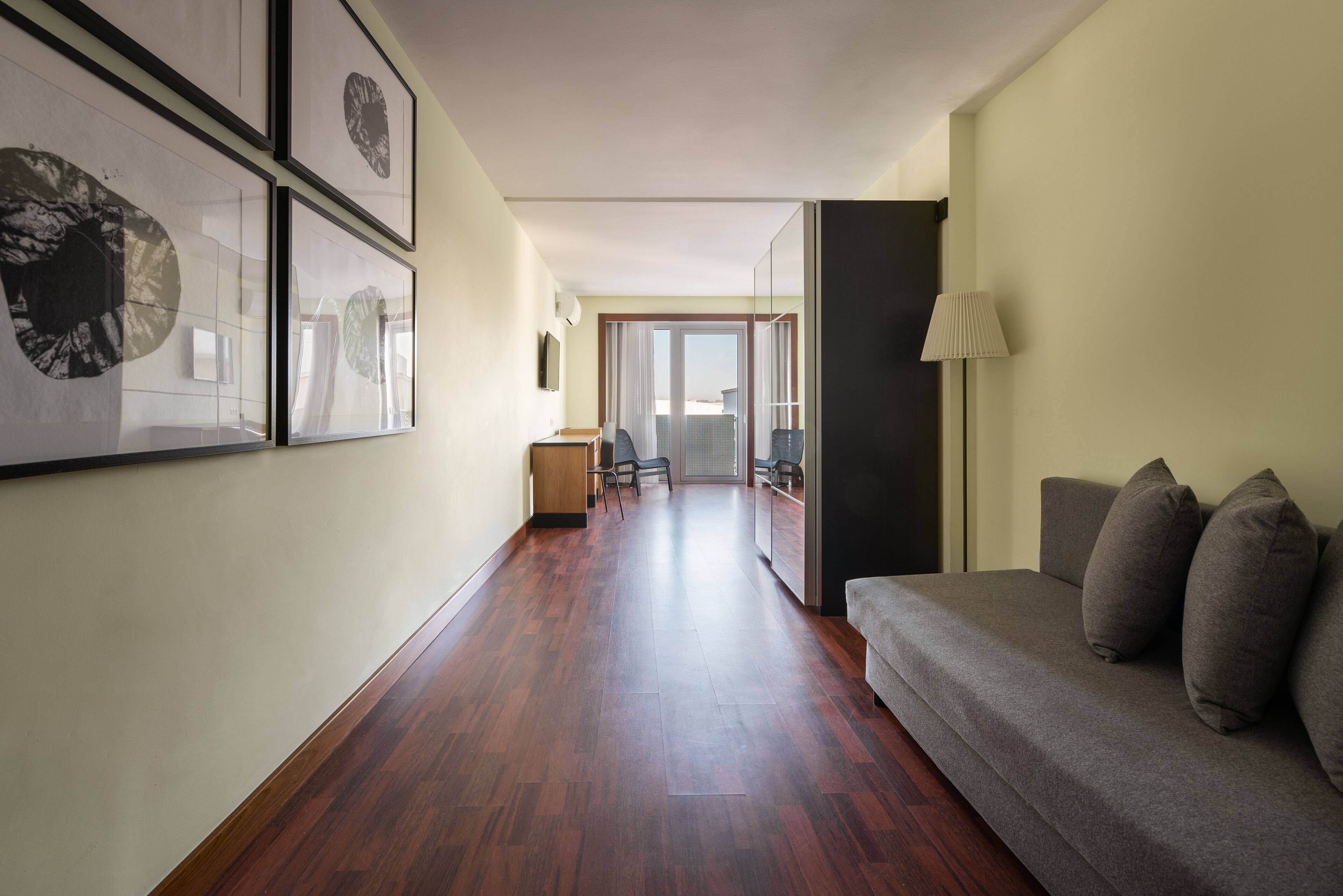 Un couloir avec un plancher en bois, un canapé avec des coussins, une lampe et des œuvres d’art encadrées accrochées au mur.