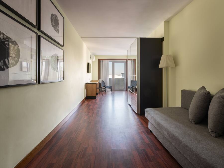 Un couloir avec un plancher en bois, un canapé avec des coussins, une lampe et des œuvres d’art encadrées accrochées au mur.