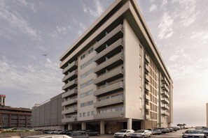 A multi-story building with balconies, a parking lot, and a clear sky.