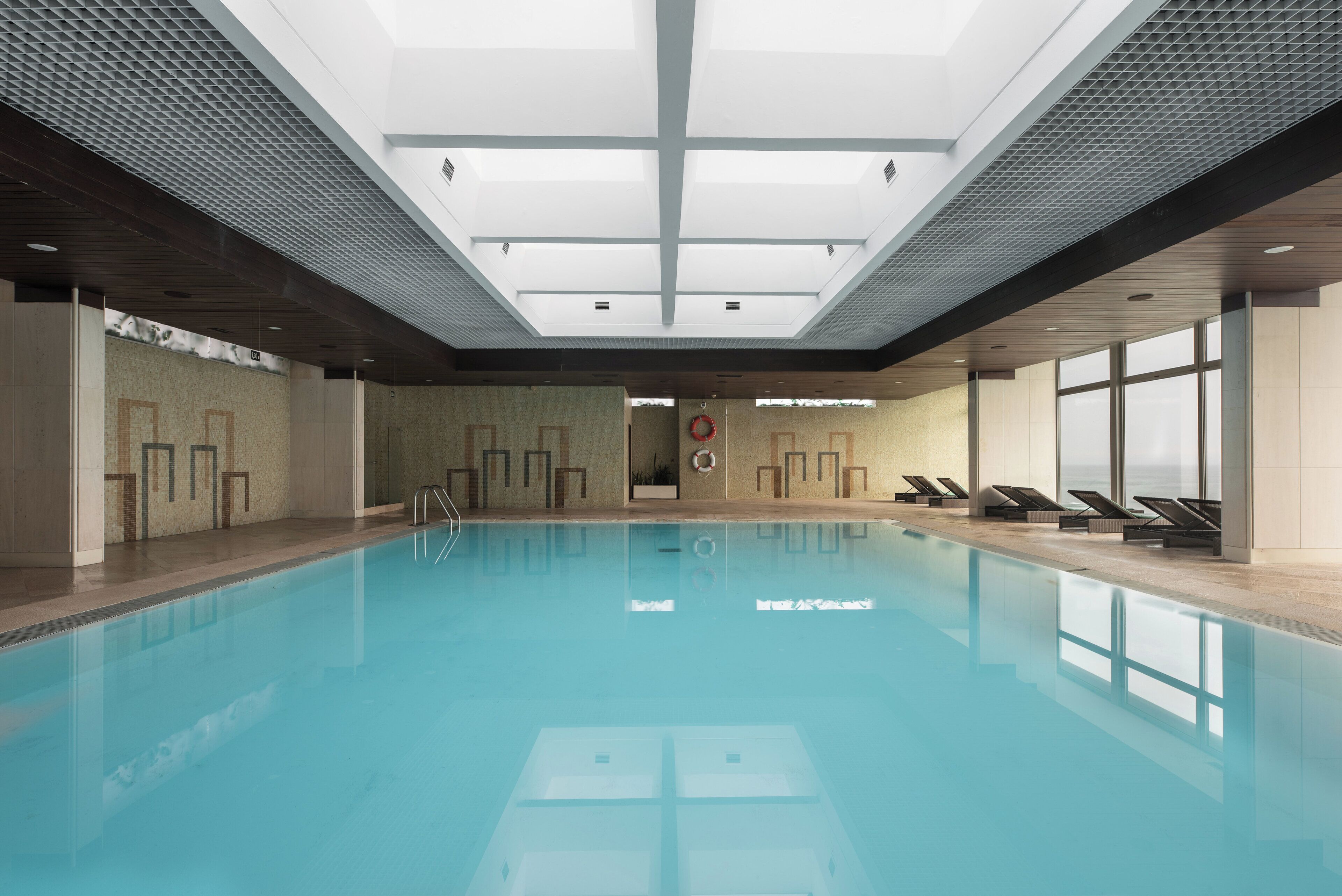 Ein moderner, überdachter Pool mit klarem, blauem Wasser und Liegestühlen am Rand.