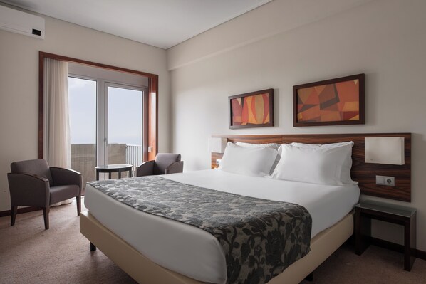 Habitación de hotel con una cama grande, dos sillones, una mesita y vistas a la ciudad desde la ventana.
