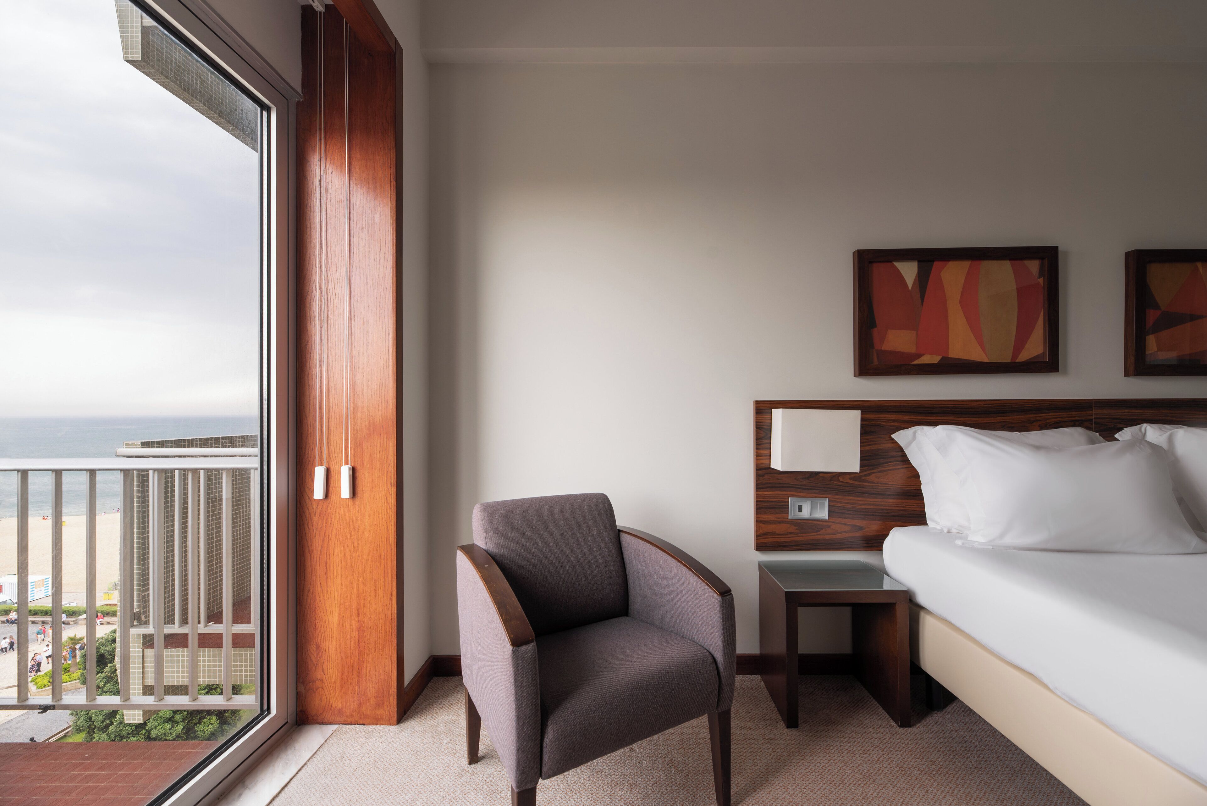 A hotel room with a bed, a chair, a nightstand, and artwork on the wall.