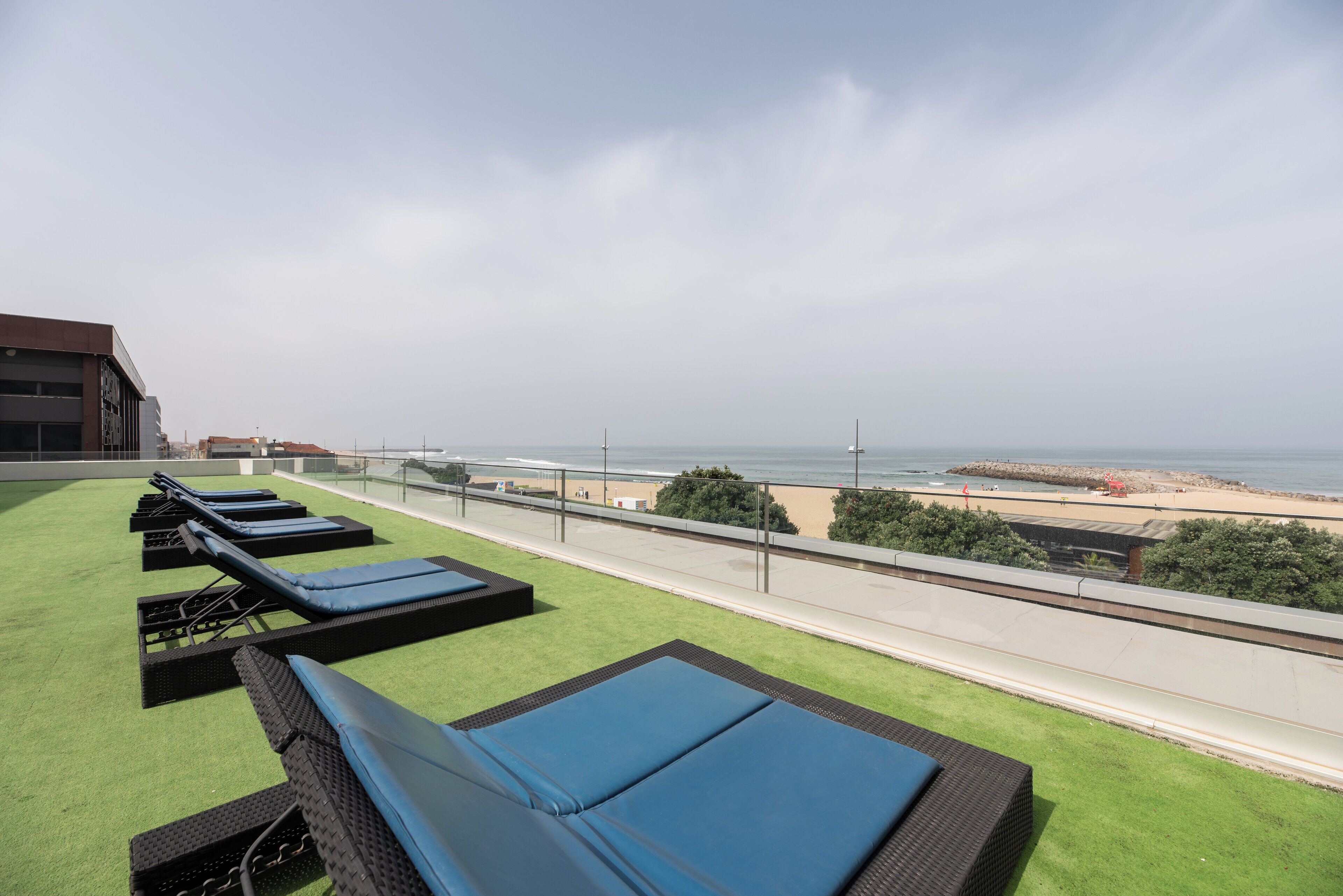 A rooftop lounge with blue cushioned loungers and a view of the beach.