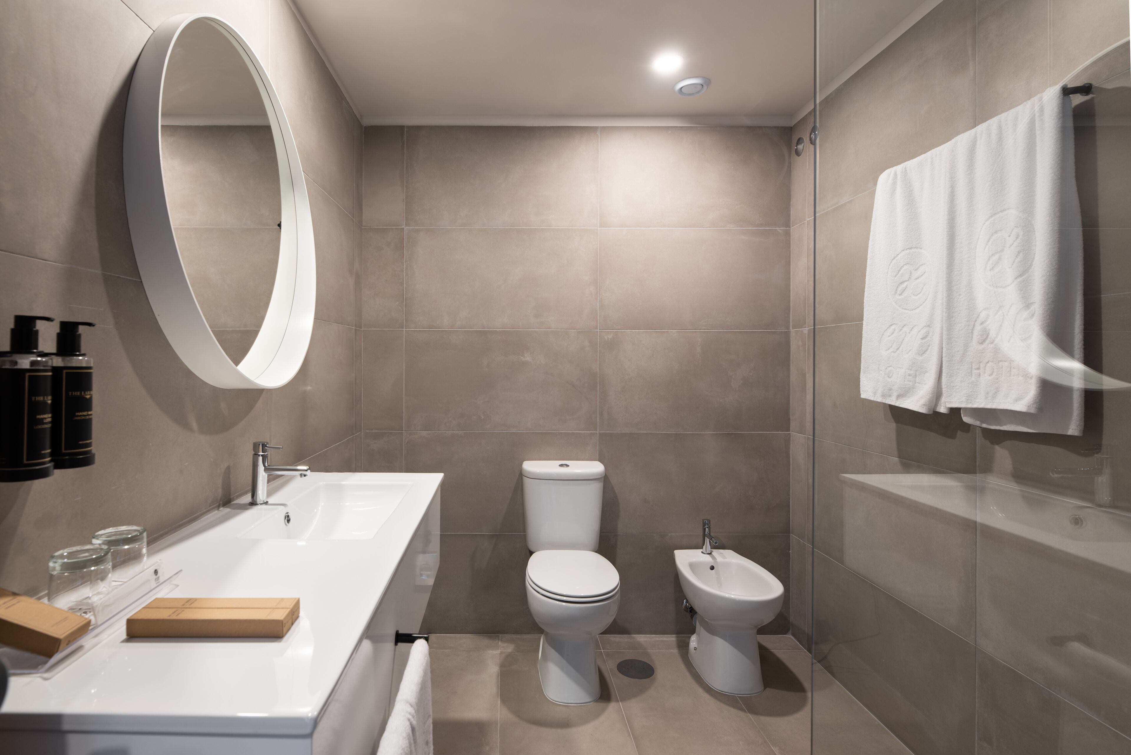 A modern bathroom with a large mirror, a white sink, a toilet, and a bidet.