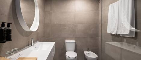 A modern bathroom with a large mirror, a white sink, a toilet, and a bidet.
