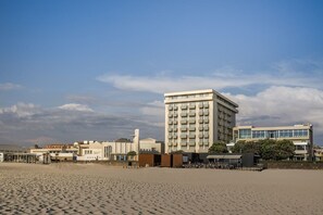 Un hôtel situé sur la côte, doté d’un bâtiment imposant, d’une plage de sable et bénéficiant d’un ciel dégagé.