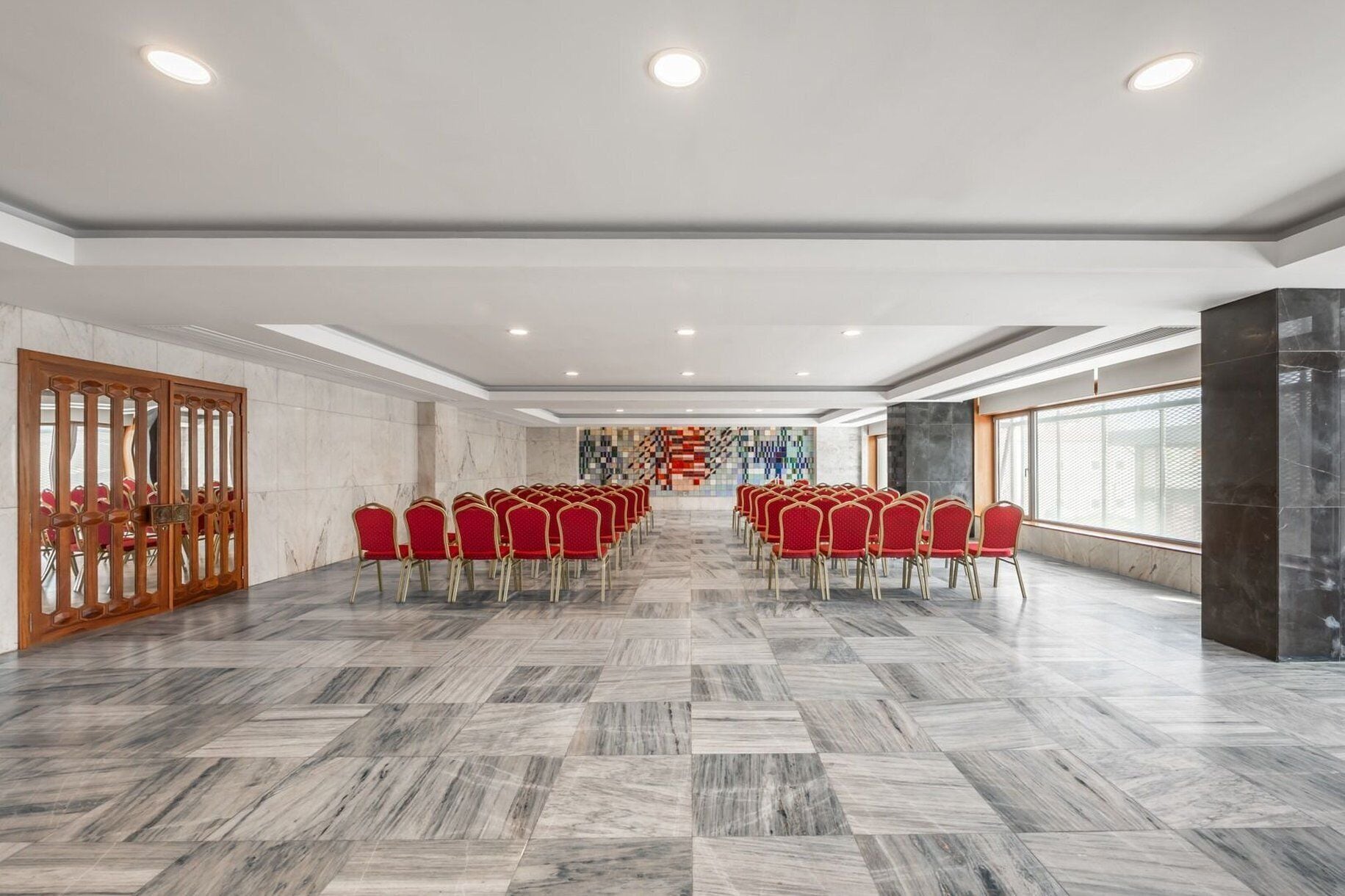 Una sala conferenze con pavimento in marmo, sedie rosse e un'ampia finestra.