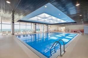 Une piscine intérieure avec une verrière, des chaises longues et une vue sur l’océan.