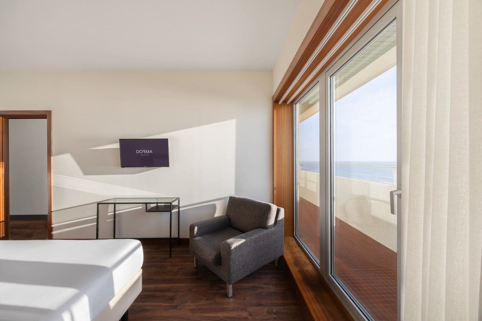 Ein Hotelzimmer mit Bett, Schreibtisch, Stuhl, Fernseher und einem großen Fenster mit Blick auf den Strand.
