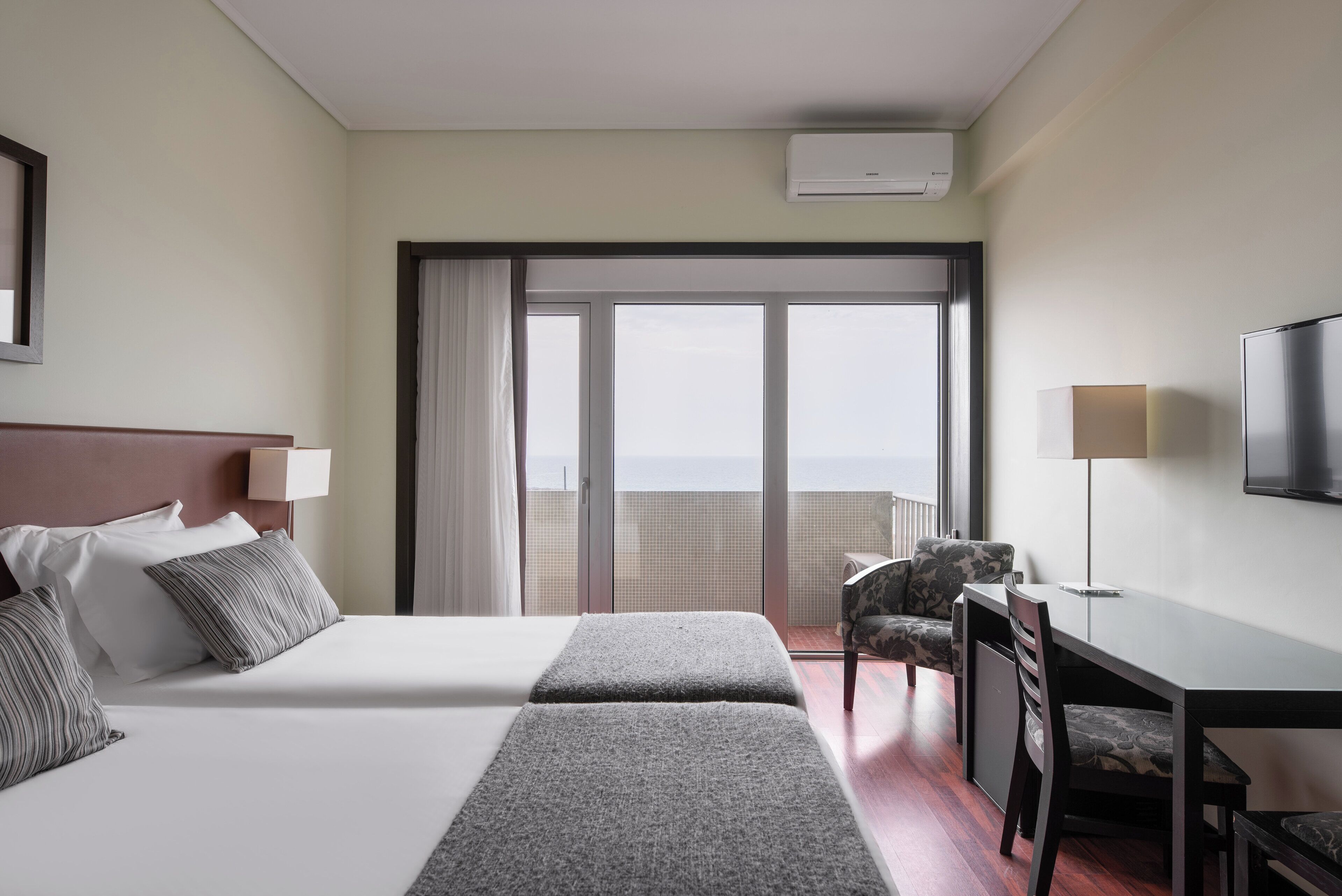 Habitación de hotel con cama, escritorio, silla, televisor y balcón con vistas.