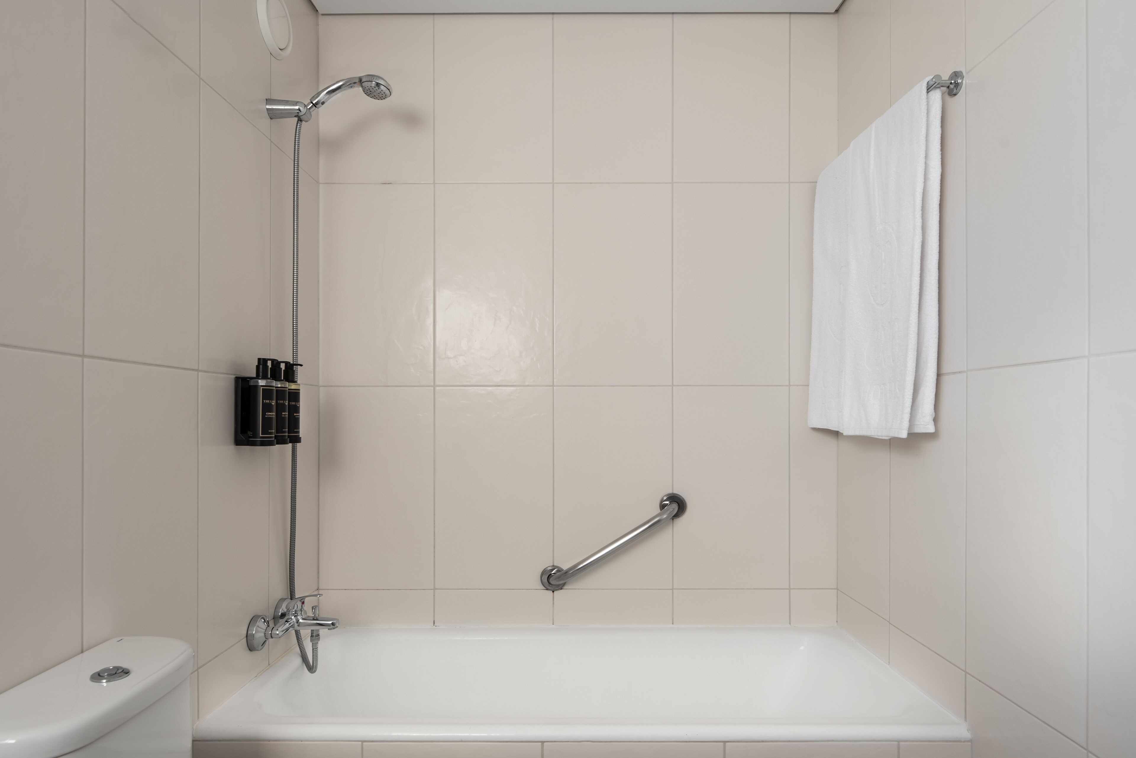 Un baño con una bañera blanca, un cabezal de ducha manual, un perchero y una barra de apoyo.