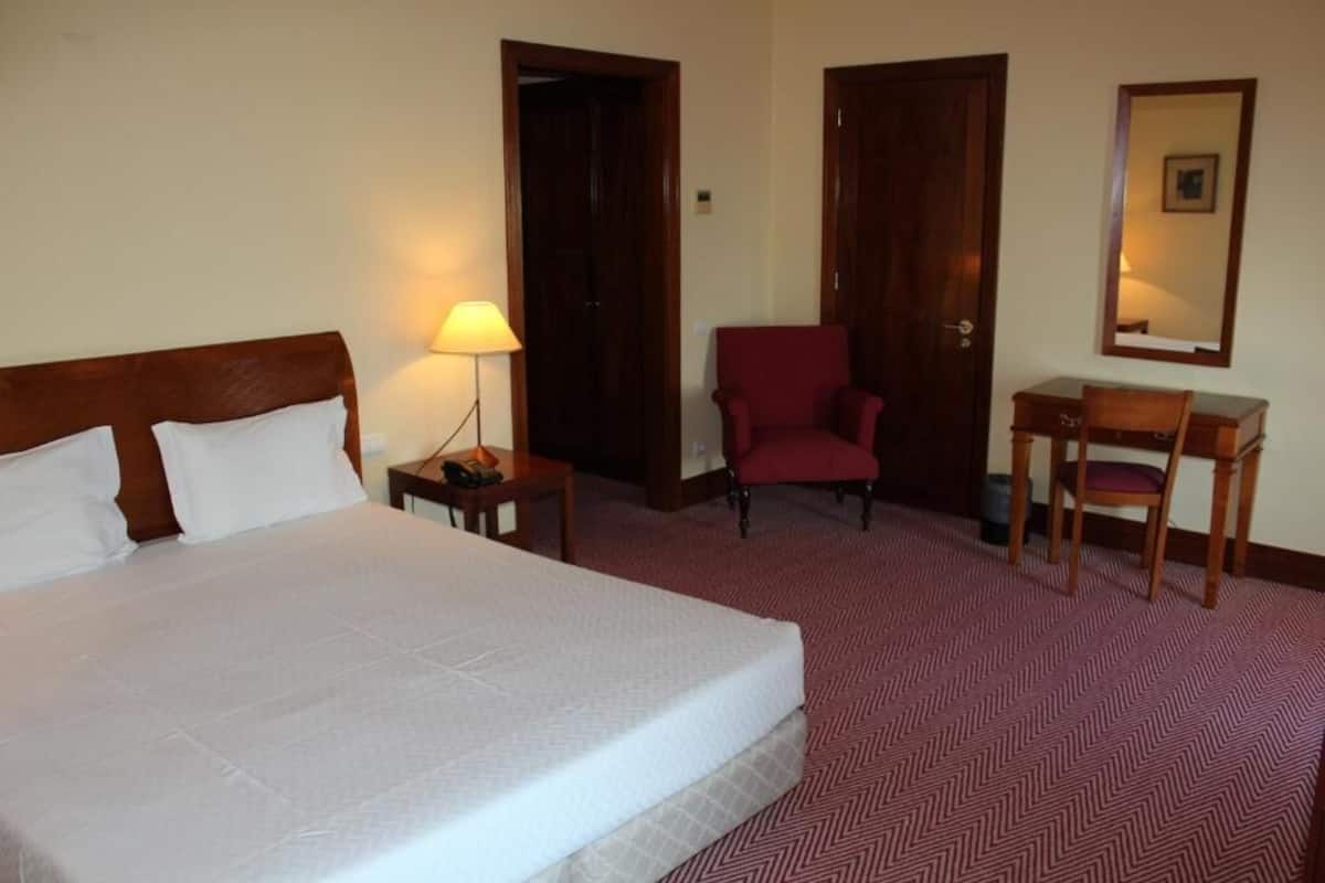 A hotel room with a large bed, a desk, a chair, and a mirror.