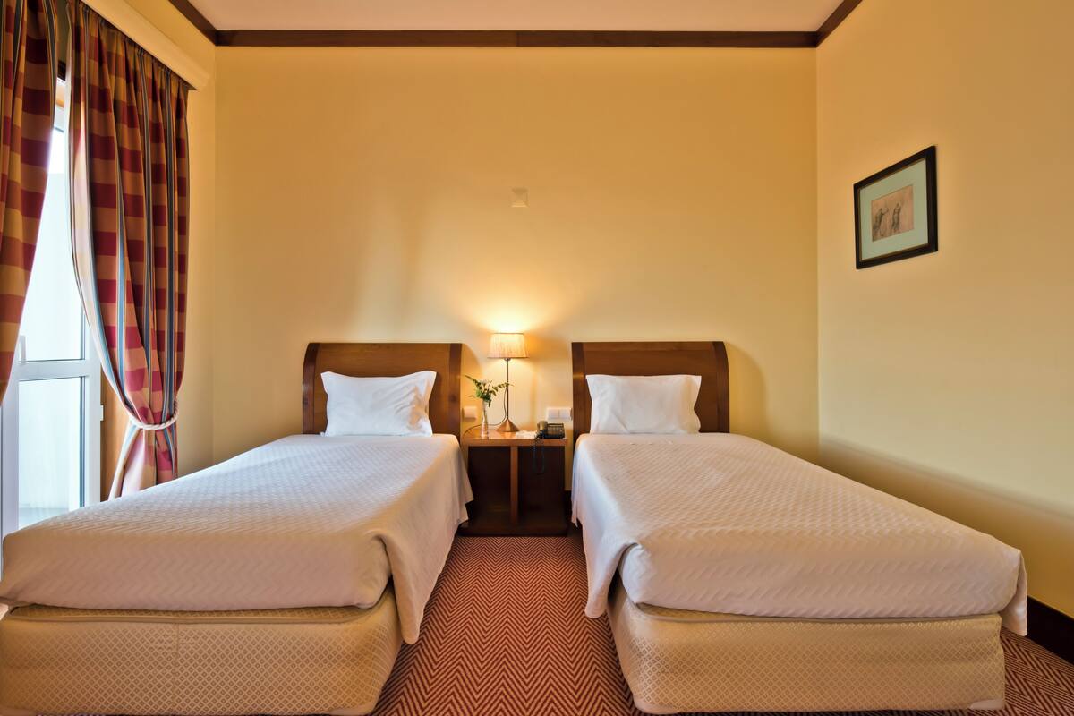 A hotel room with two beds, a nightstand, a lamp, and a framed picture on the wall.