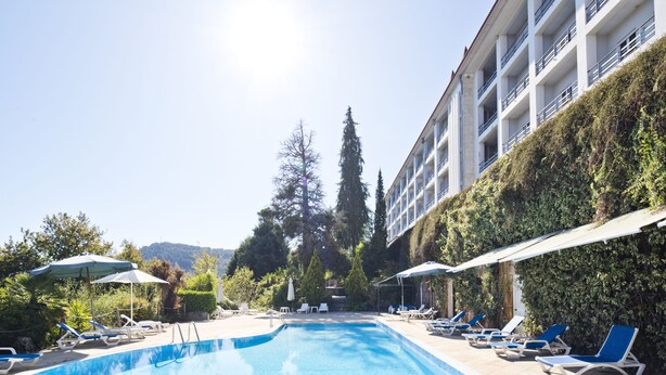A swimming pool with lounge chairs and umbrellas, surrounded by greenery and a building with balconies. - Lam Hotel Caramulo  (Tondela)