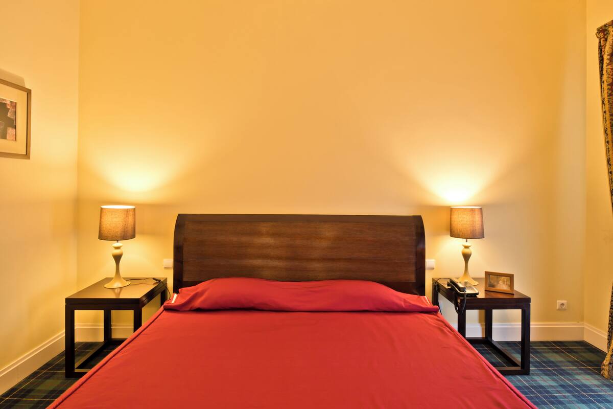 A hotel room with a bed, two bedside tables with lamps, a telephone, and a picture frame on one of the tables.