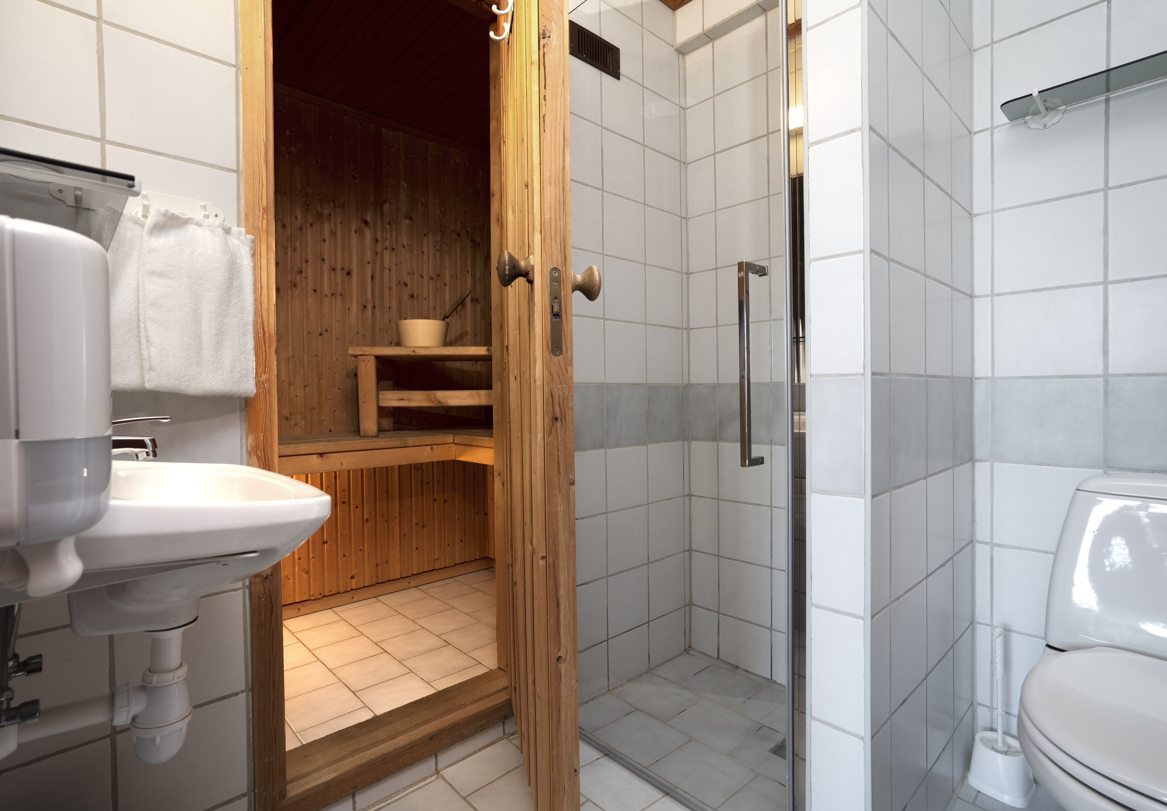 Et badeværelse med brusekabine i træ, vask og toilet.
