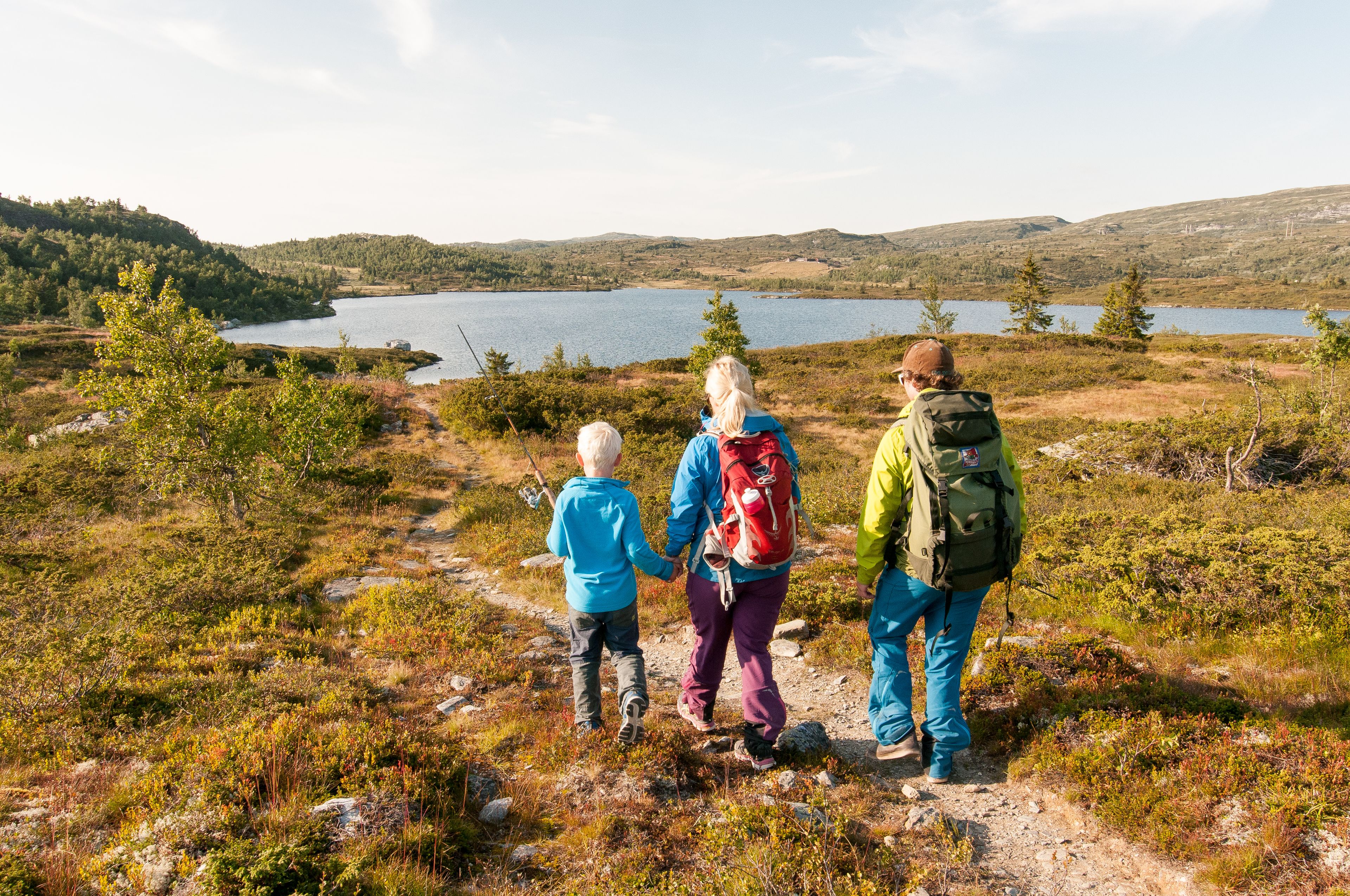 A group of people hiking on a trail with a lake and hills in the background.