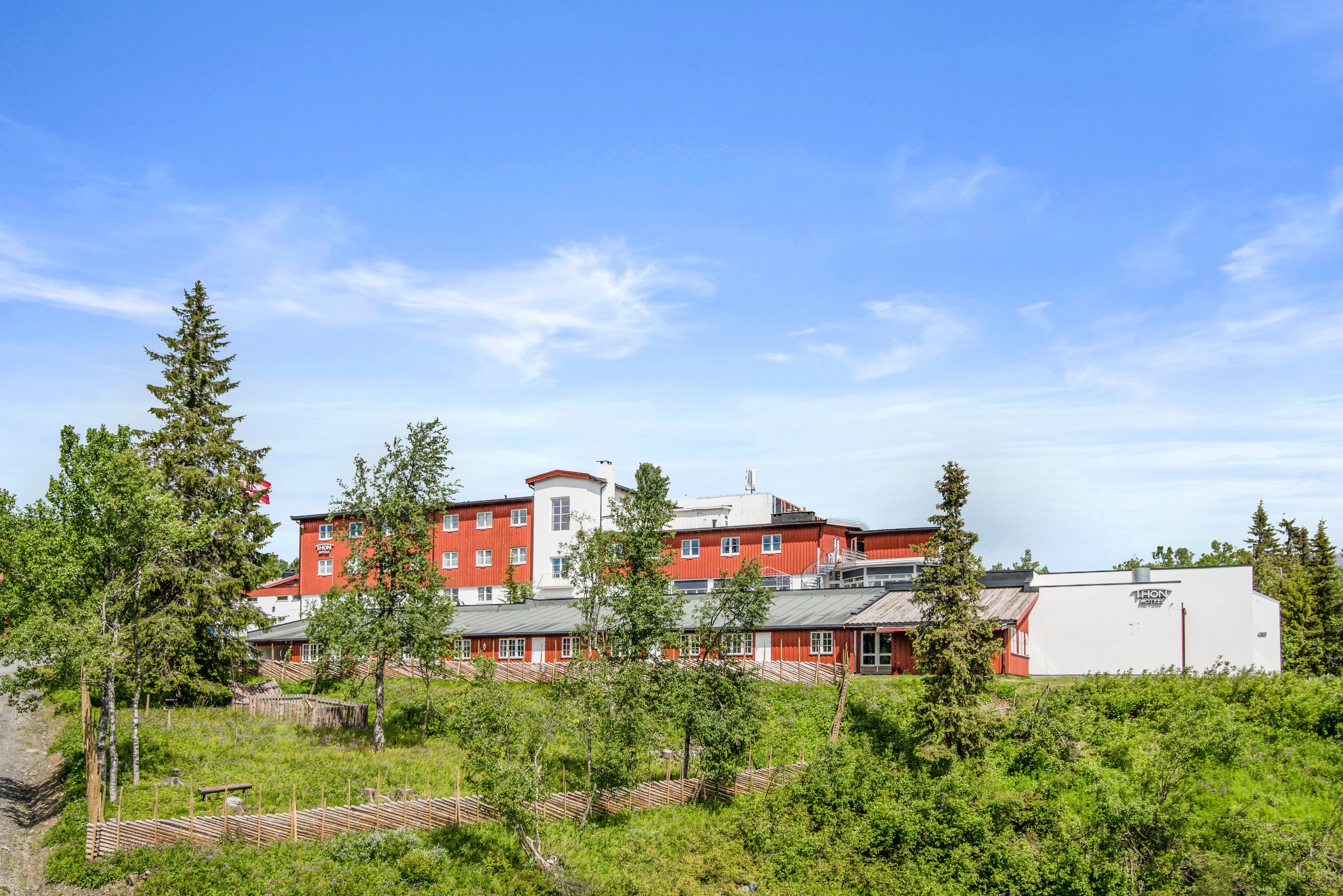 Un edificio a più piani con facciata rossa e bianca, circondato da vegetazione e alberi.