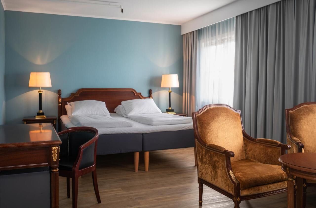 Et hotelværelse med en dobbeltseng, to sengeborde med lamper, et skrivebord, en stol og et spisebord.