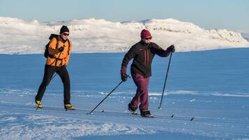 Two people cross-country skiing on a snowy landscape with mountains in the background.