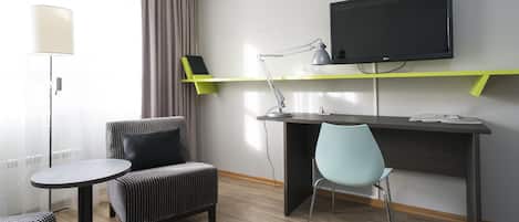 Una habitación de hotel moderna con escritorio, dos sillas, televisor y lámpara.