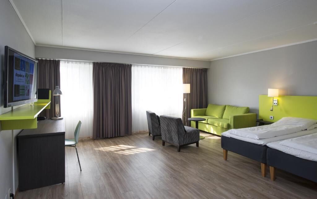 Una habitación de hotel con escritorio, dos sillas, un sofá, una cama y un televisor.