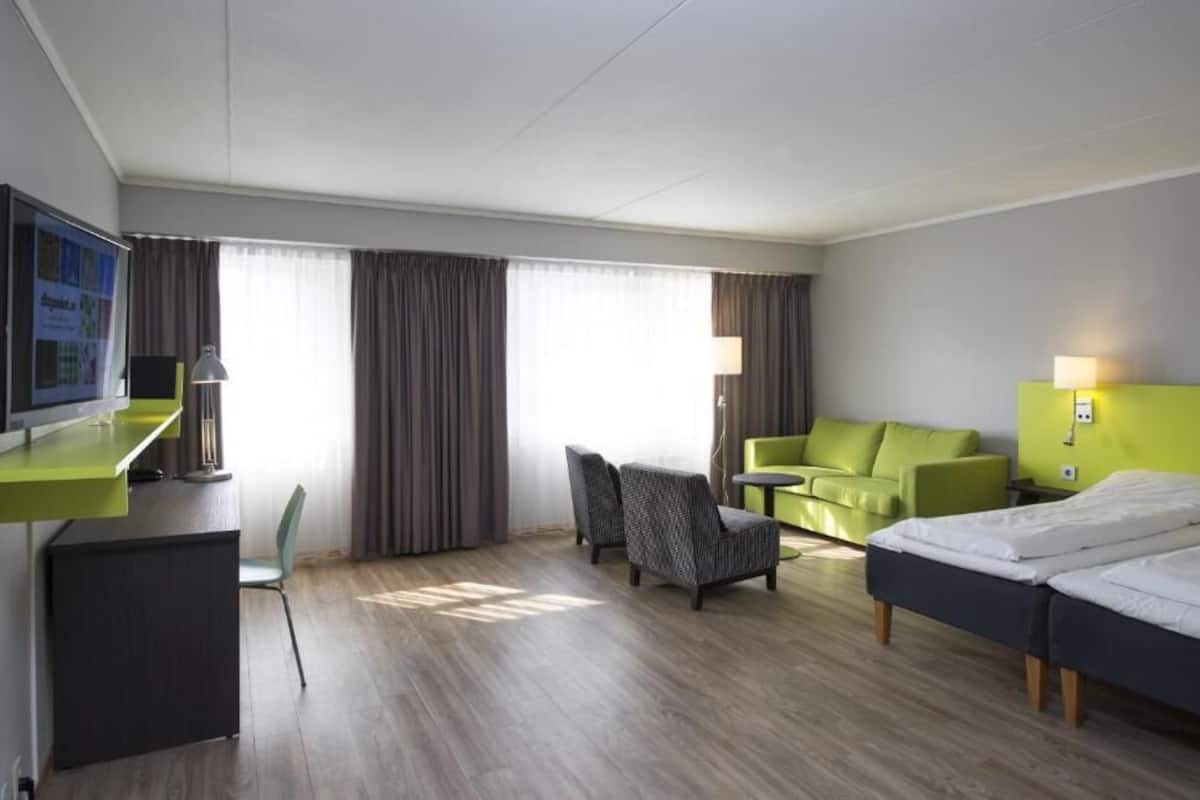 A hotel room with a desk, two chairs, a sofa, a bed, and a TV.