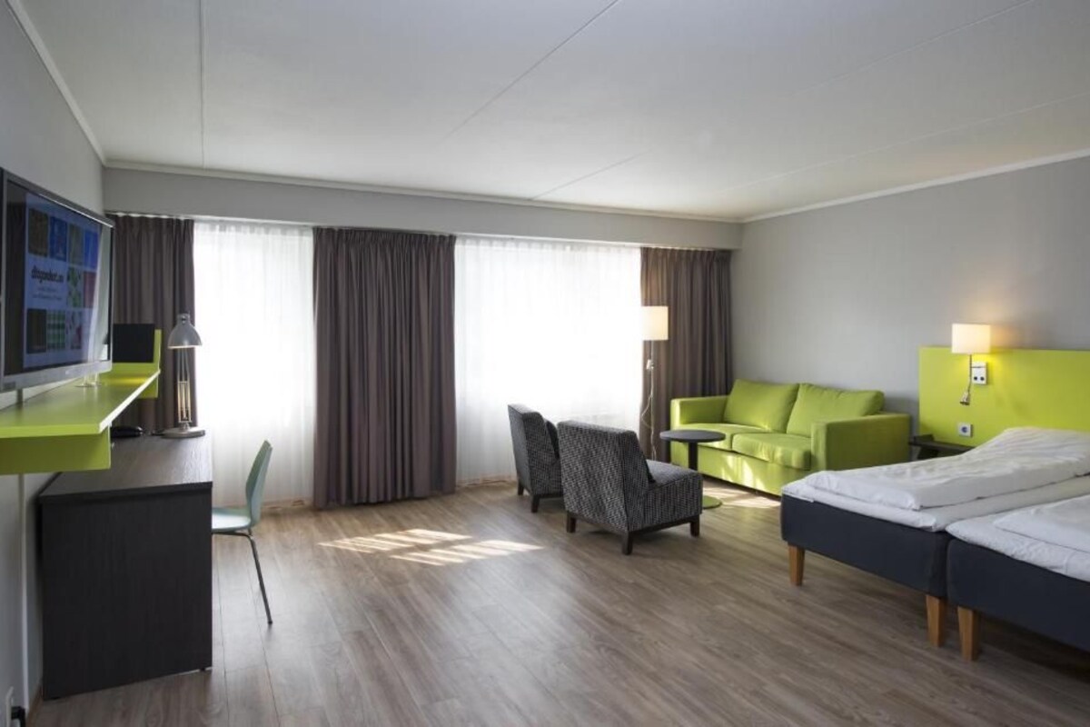 A hotel room with a desk, two chairs, a sofa, a bed, and a TV.