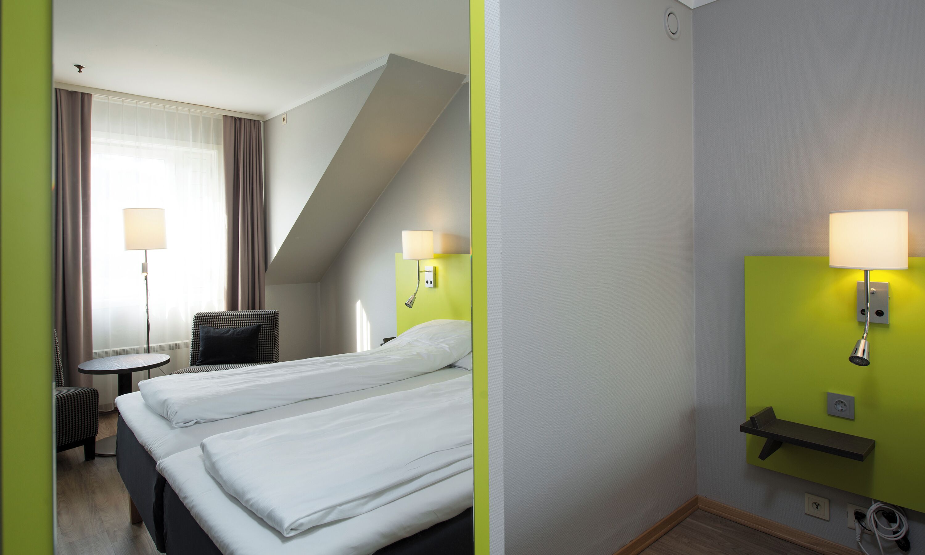 Une chambre d’hôtel avec deux lits, une chaise, une petite table et une lampe.