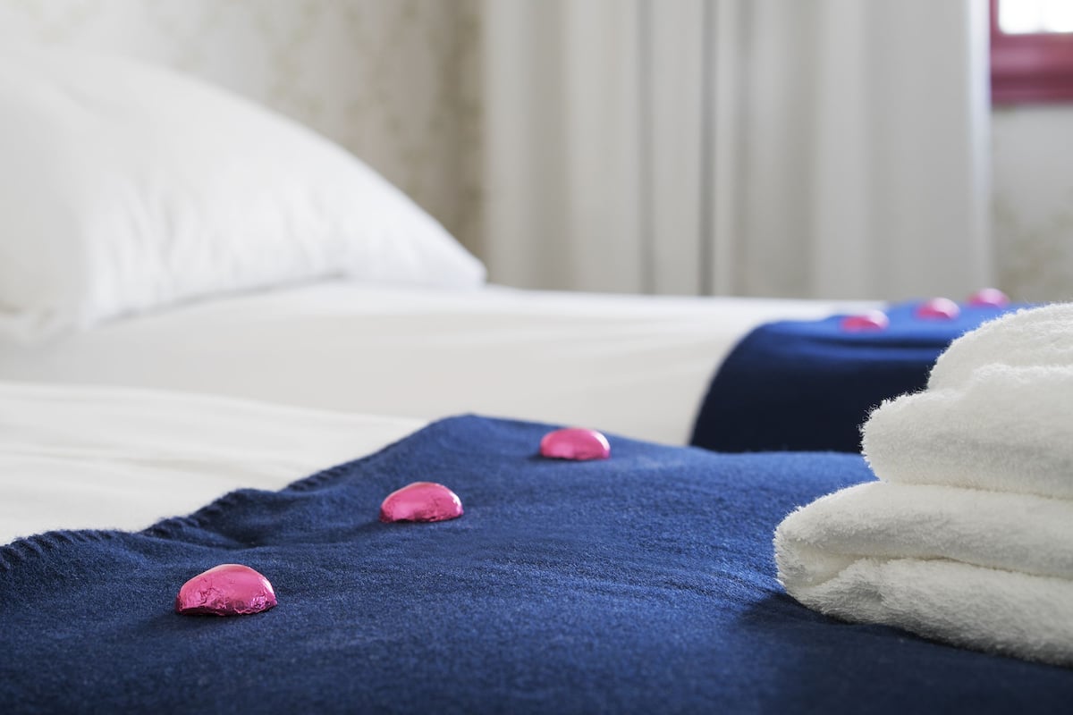A neatly made bed with a blue blanket and pink bath salts.