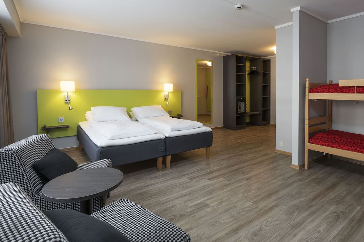 A hotel room with a bed, a sofa, a small table, and a bunk bed.
