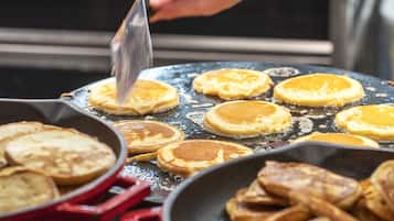 A kitchen with pancakes being cooked on a griddle.