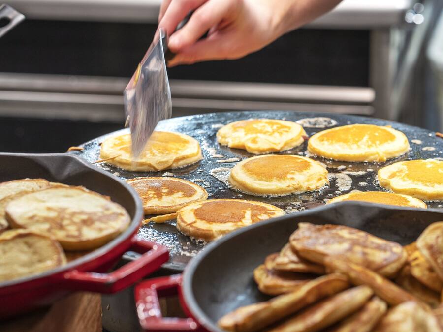 A kitchen with pancakes being cooked on a griddle.
