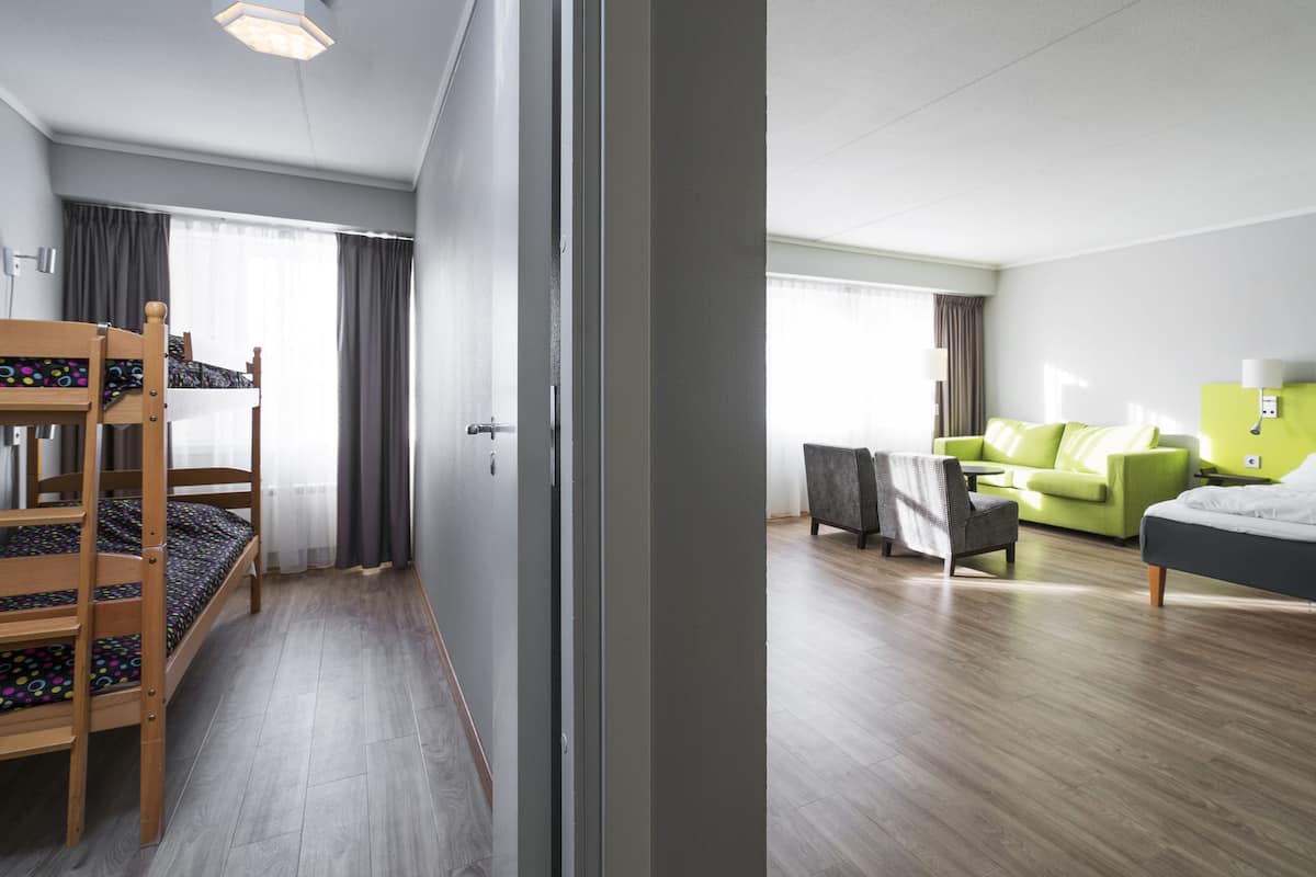 A hotel room with bunk beds, a green sofa, a bed with white bedding, and a wooden floor.