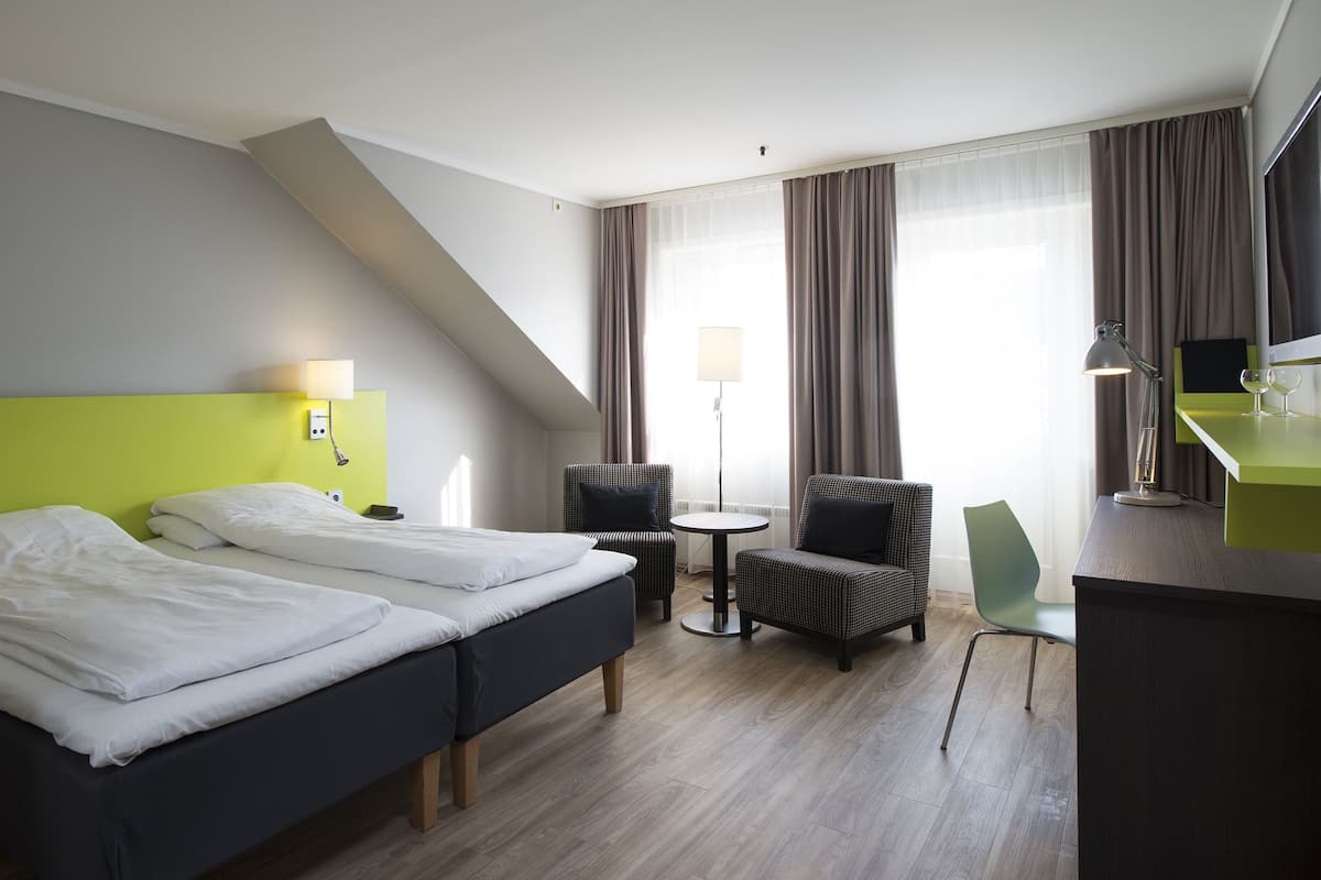 A hotel room with two beds, a desk, a chair, a lamp, and a TV.