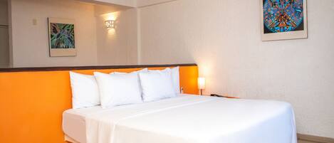 Una habitación de hotel con una cama, una mesita de noche, una lámpara de pared y dos cuadros decorativos.
