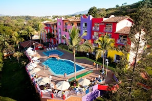 Un hotel colorido con piscina rodeada de palmeras y sillas de descanso.