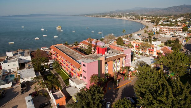 Un pueblo costero con un edificio rosa destacado, una playa y varias embarcaciones en el agua.