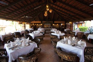 Un espace de restauration intérieur avec des tables dressées, des chaises en bois et un plafond haut orné de luminaires suspendus.