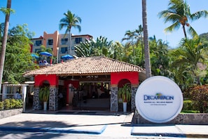Entrada a un resort con un edificio rojo y blanco, palmeras y un letrero de Decameron.