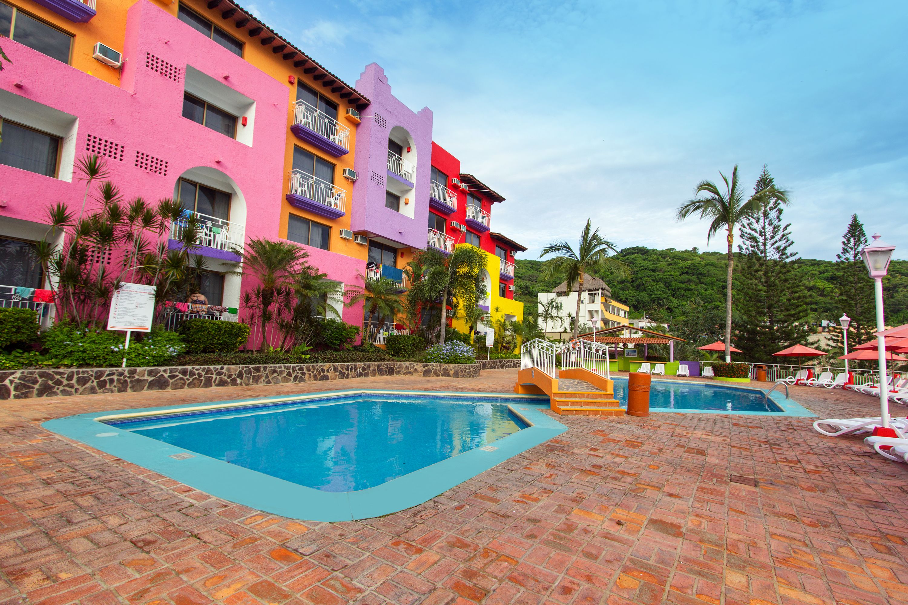 A hotel with colorful exterior walls, a swimming pool, and a brick patio area.