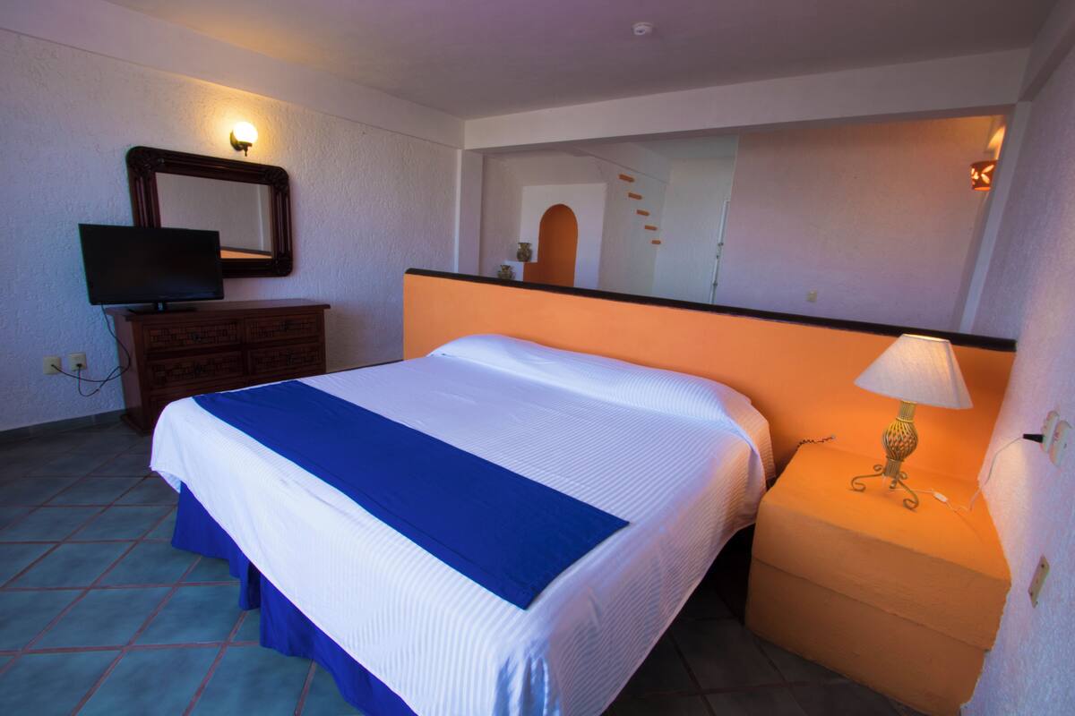 A hotel room with a large bed, a dresser, a television, and a mirror.