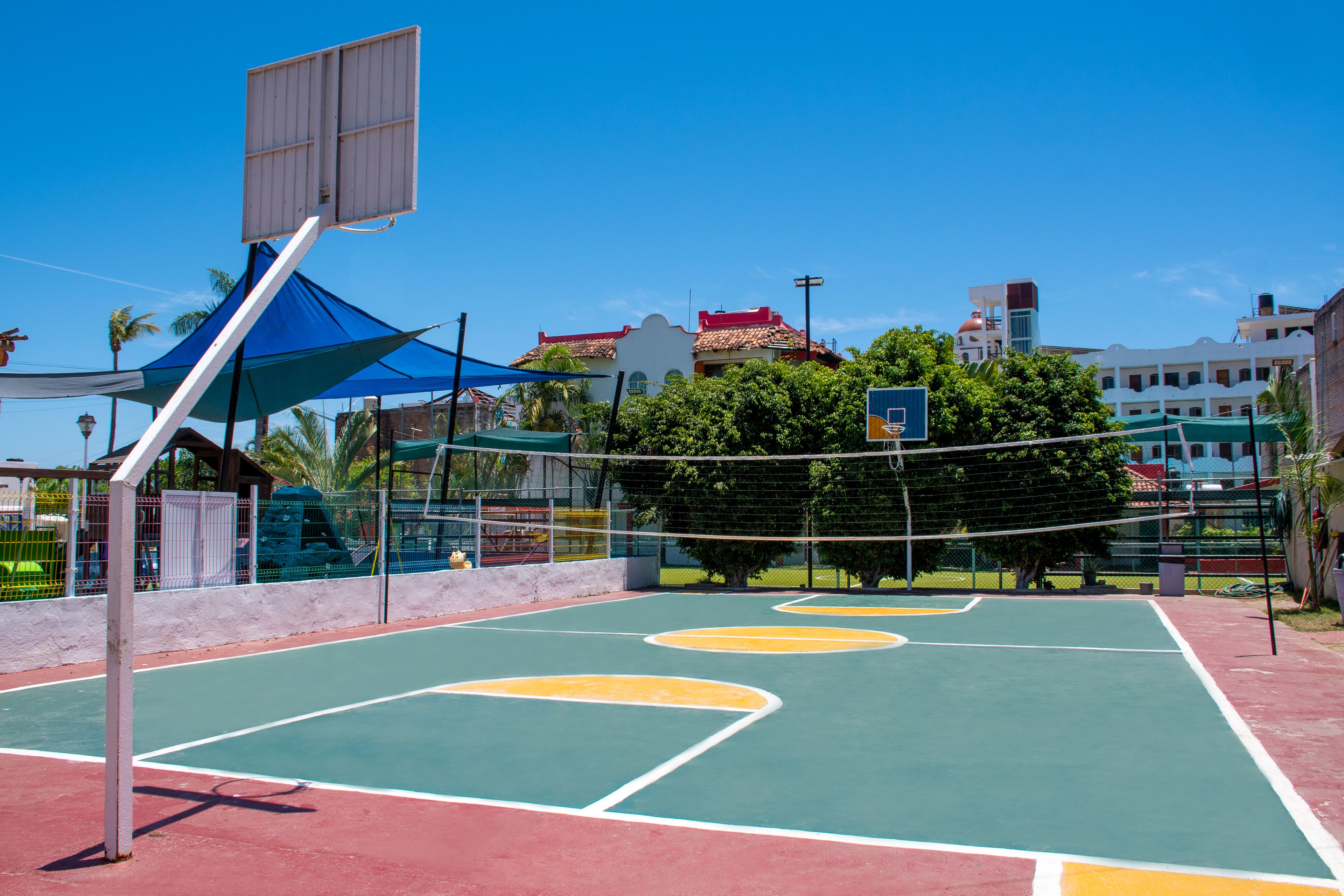 Una cancha de baloncesto al aire libre con red, aro y una estructura azul de sombra.